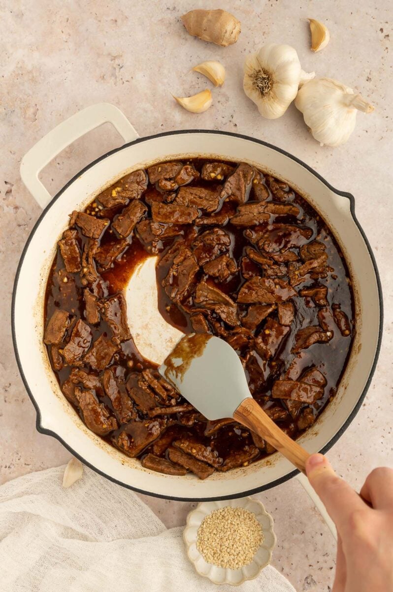 A spatula stirring beef in a stir fry sauce in a skillet.