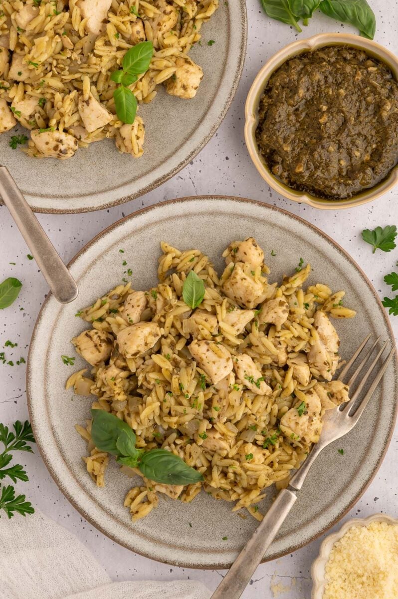 A grey plate with a helping of pesto chicken orzo with a fork on it. 
