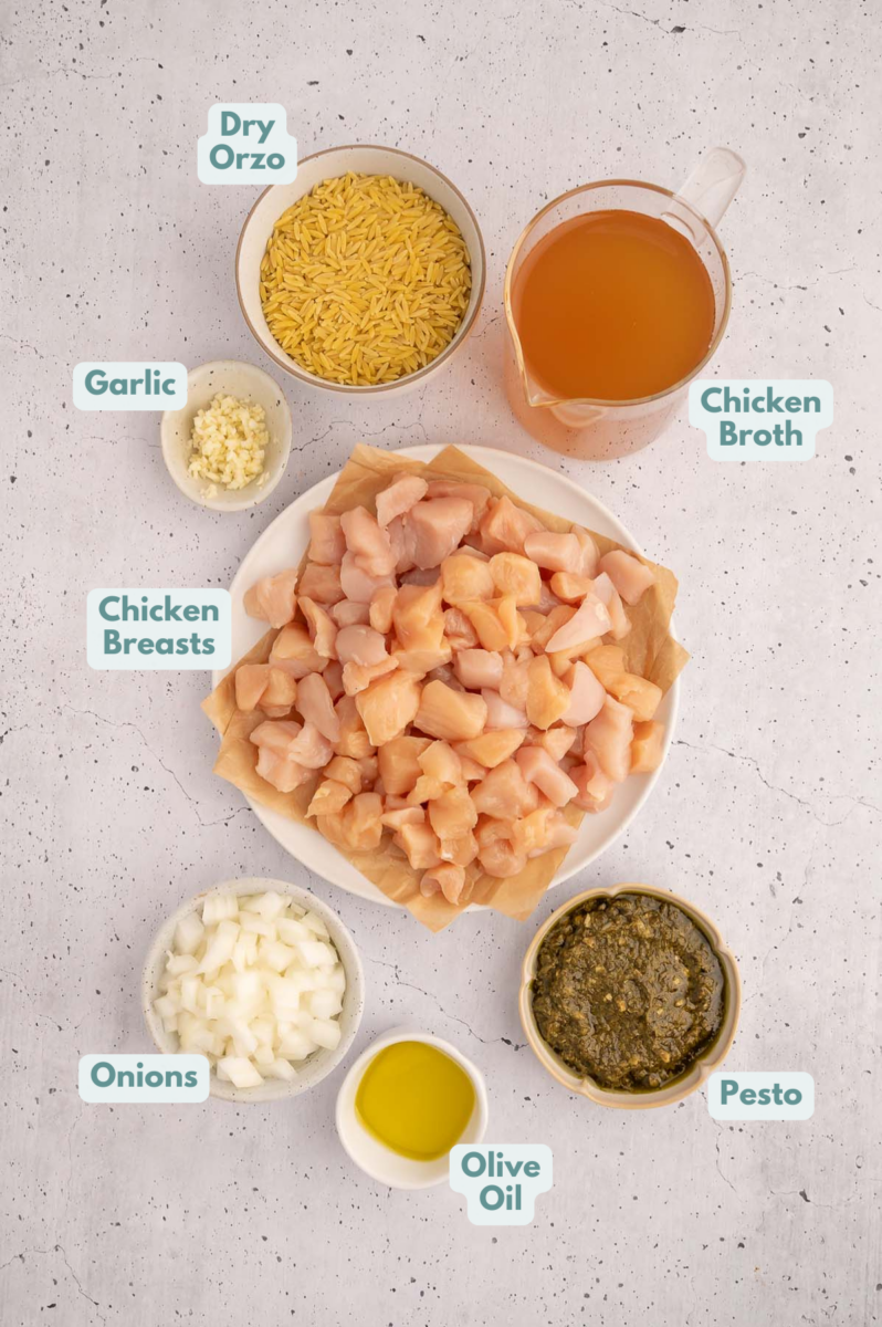 Ingredients to make pesto chicken orzo in bowls and measuring cups on a counter.