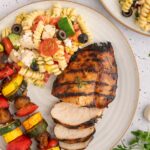 Balsamic grilled chicken on a plate with pasta salad and grilled veggie kebabs.