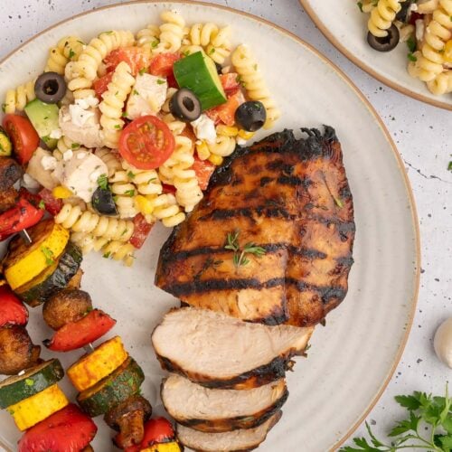 Balsamic grilled chicken on a plate with pasta salad and grilled veggie kebabs.