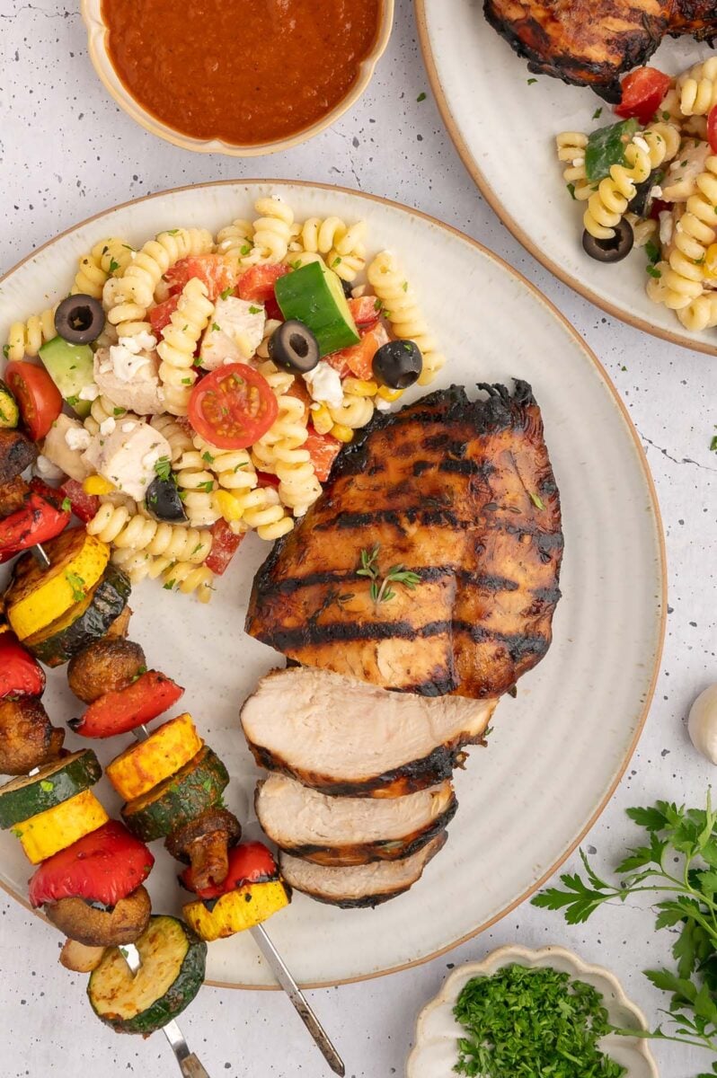 Balsamic grilled chicken on a plate with pasta salad and grilled veggie kebabs.