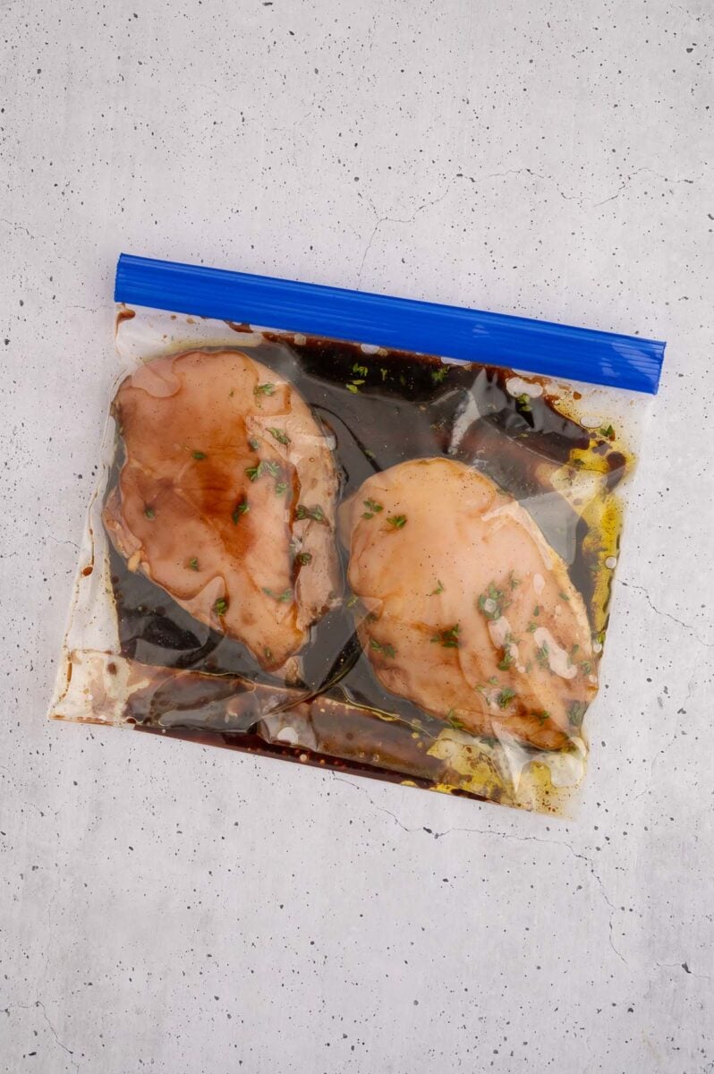 Two raw chicken breasts in a bag marinating in balsamic marinade. 