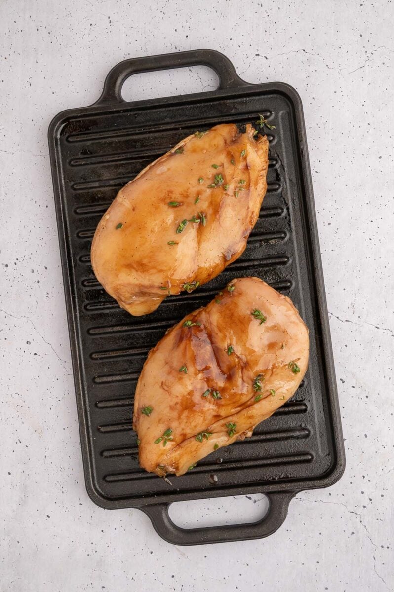 Raw balsamic chicken breasts on a black stovetop grill pan. 