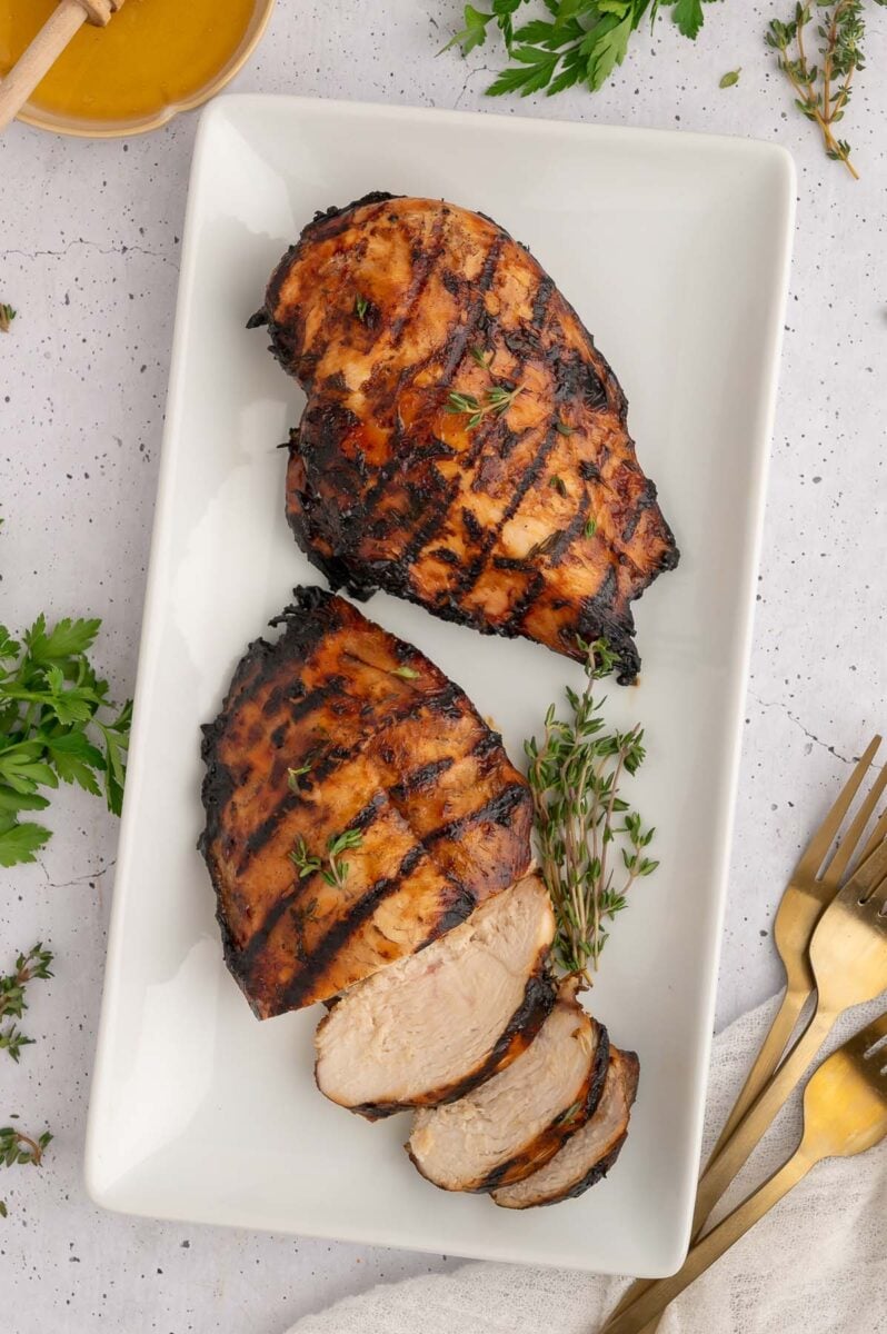 Balsamic grilled chicken on a white platter. One is sliced. 