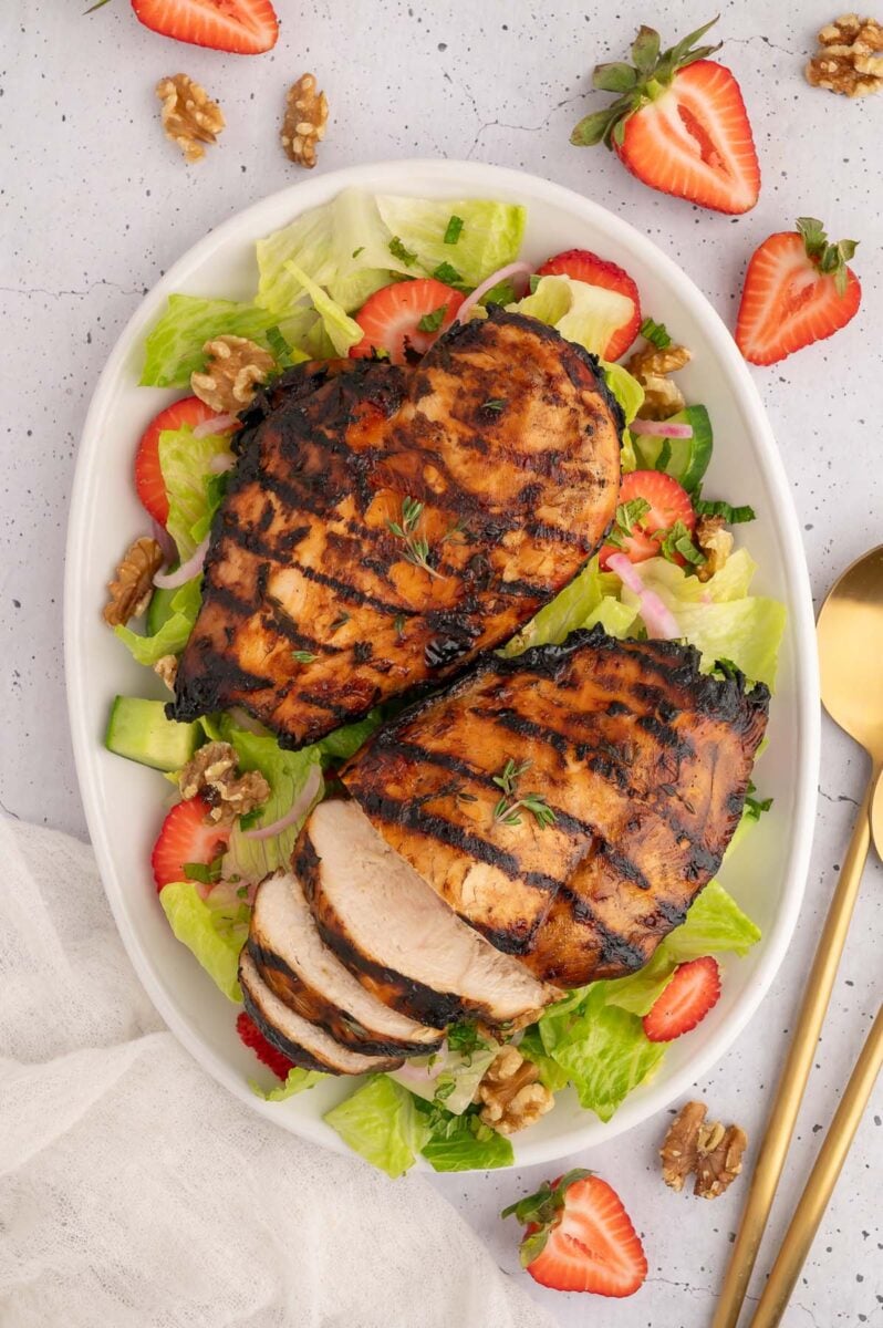 Two balsamic grilled chicken breasts on a salad on a platter. 