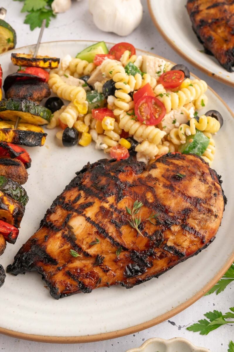 A grilled balsamic chicken breast with veggie kebabs and pasta salad. 