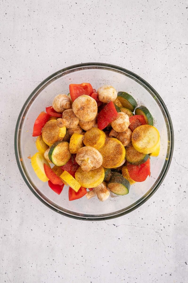 Chopped veggies in a bowl tossed in olive oil and seasonings. 