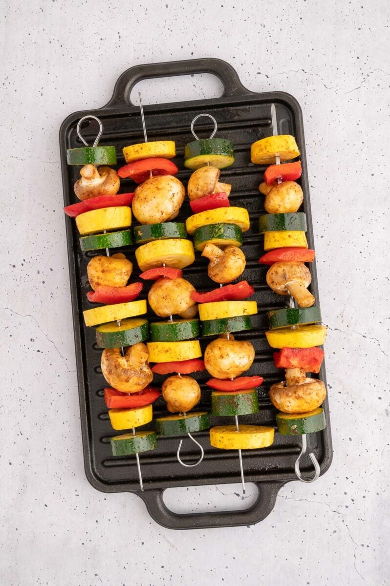 Uncooked veggie kebabs on a stovetop grill. 