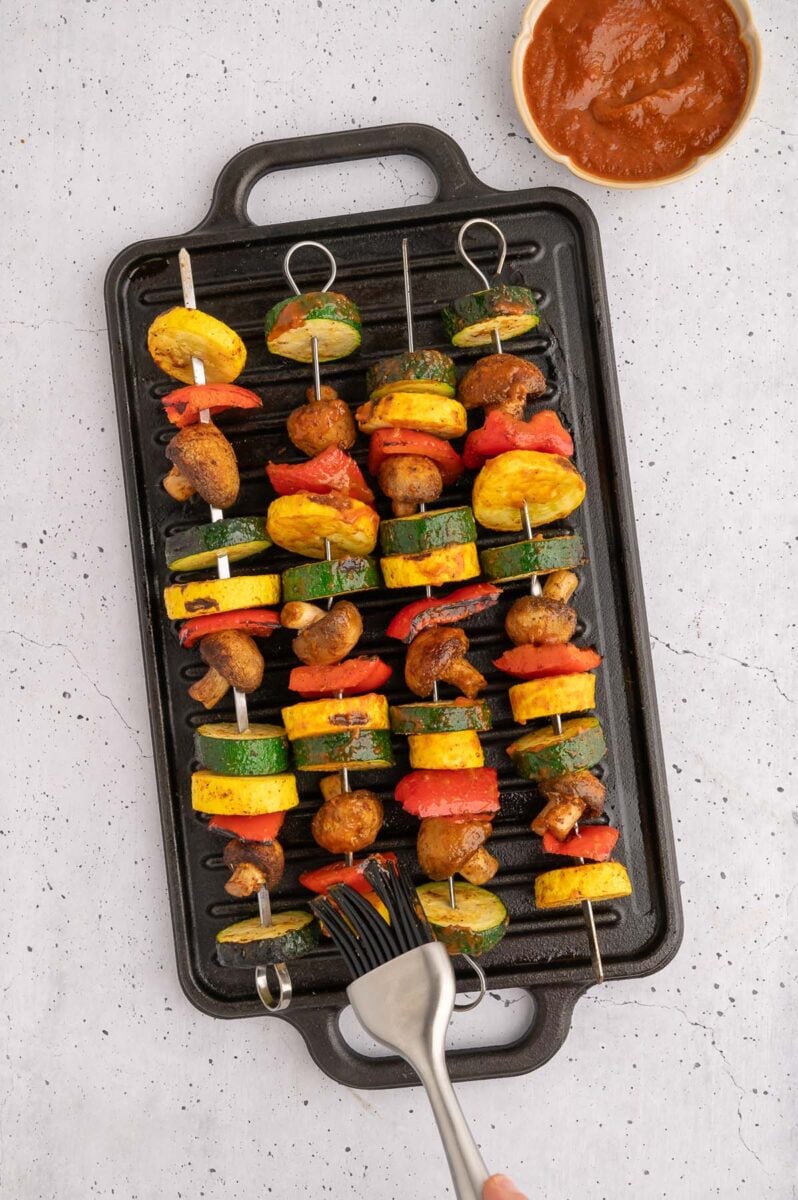 BBQ grilled vegetables on a stovetop grill with bbq sauce on the side. 