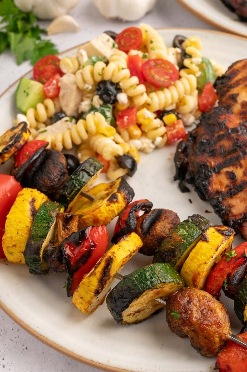 Grilled bbq vegetables on a plate with pasta salad and balsamic grilled chicken. 