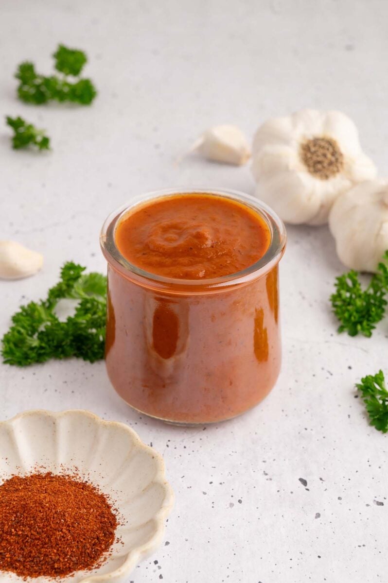 A small glass jar filled with healthy bbq sauce with spices and garlic on the side.