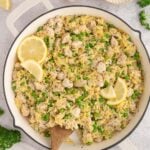 Lemon Chicken Orzo in a skillet with a wooden spoon in it garnished with lemon slices.