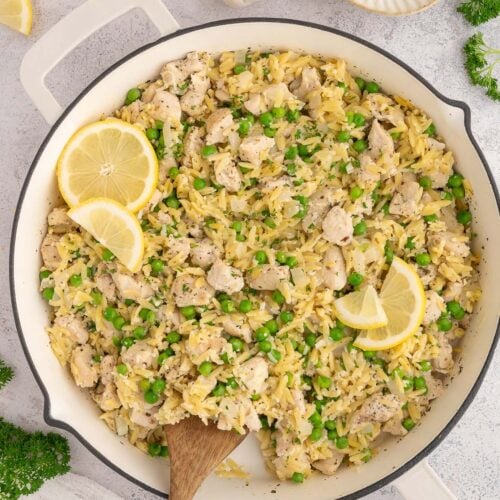 Lemon Chicken Orzo in a skillet with a wooden spoon in it garnished with lemon slices.
