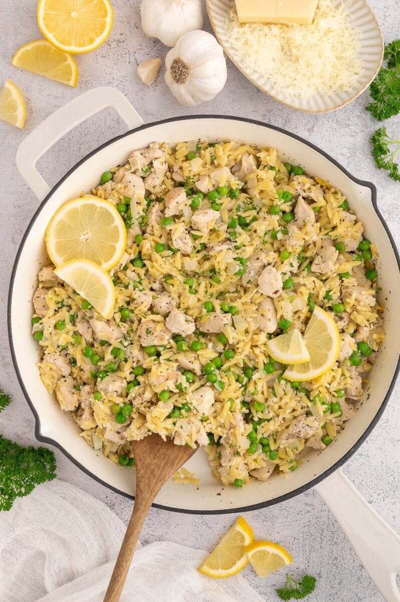 Lemon Chicken Orzo in a skillet with a wooden spoon in it garnished with lemon slices.