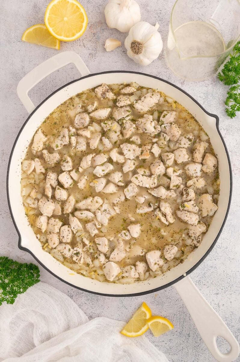 Cooked chicken pieces and orzo in chicken broth in a skillet.