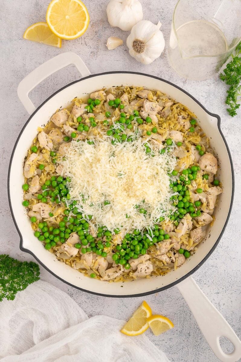Peas and parmesan on chicken orzo in a skillet before mixing together.