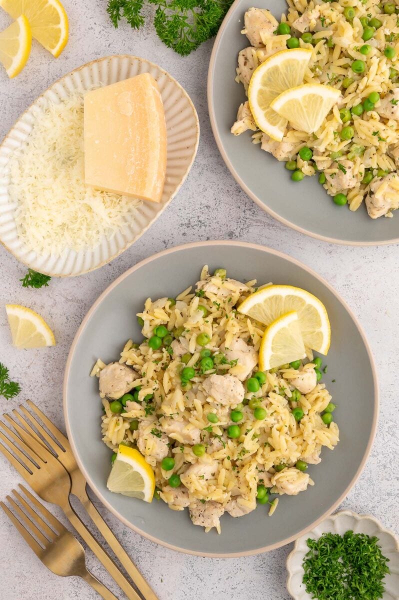 Two grey plates with a serving of lemon chicken orzo on them with grated parmesan on the side.