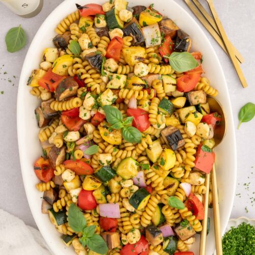 Grilled Vegetable Pasta Salad on a white platter with gold spoons in it.