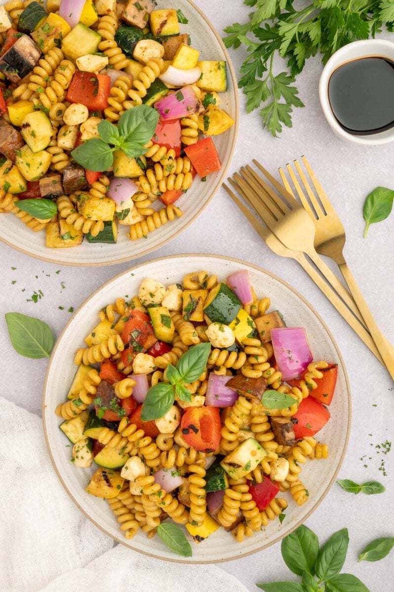 Grilled Vegetable Pasta Salad on two plates with gold forks on the side.