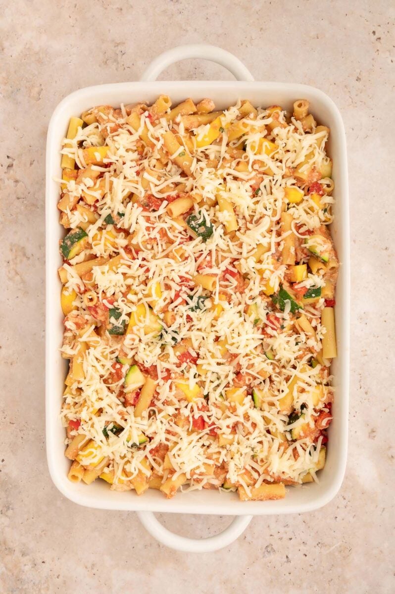 Uncooked vegetable baked ziti in a baking dish topped with mozzarella cheese.