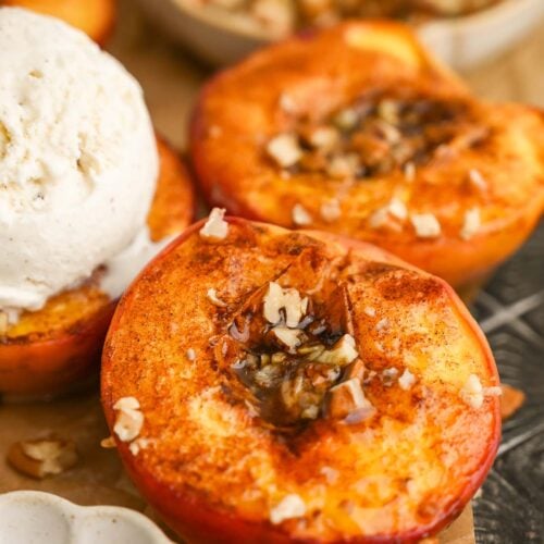 Close up of baked peaches with a scoop of ice cream in the background.