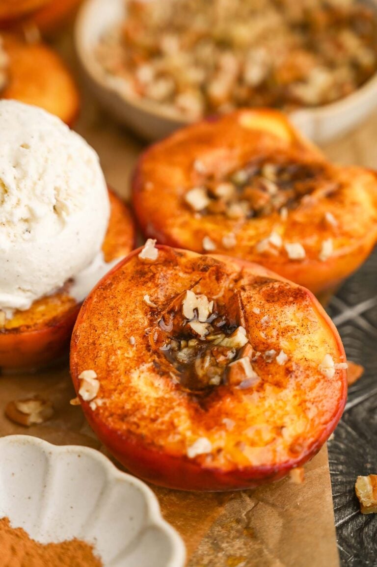 Close up of baked peaches with a scoop of ice cream in the background.