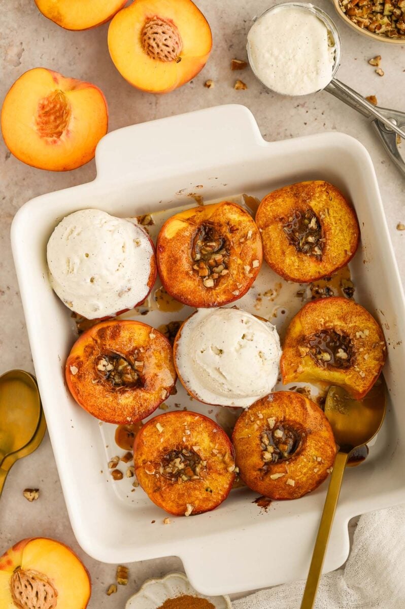 Baked peaches in a baking dish with scoops of ice cream in it too.
