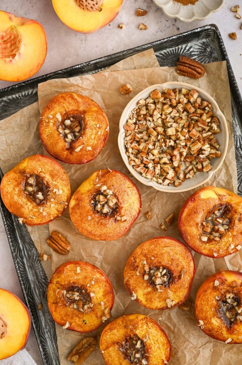 Baked peaches on a baking sheet with chopped pecans on them.