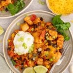 Chicken Taco Rice on a plate with limes, cilantro and a dollop of sour cream on it.