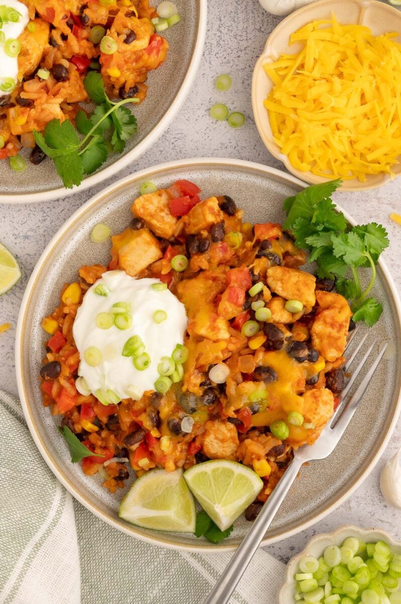 Chicken Taco Rice on a plate with limes, cilantro and a dollop of sour cream on it.