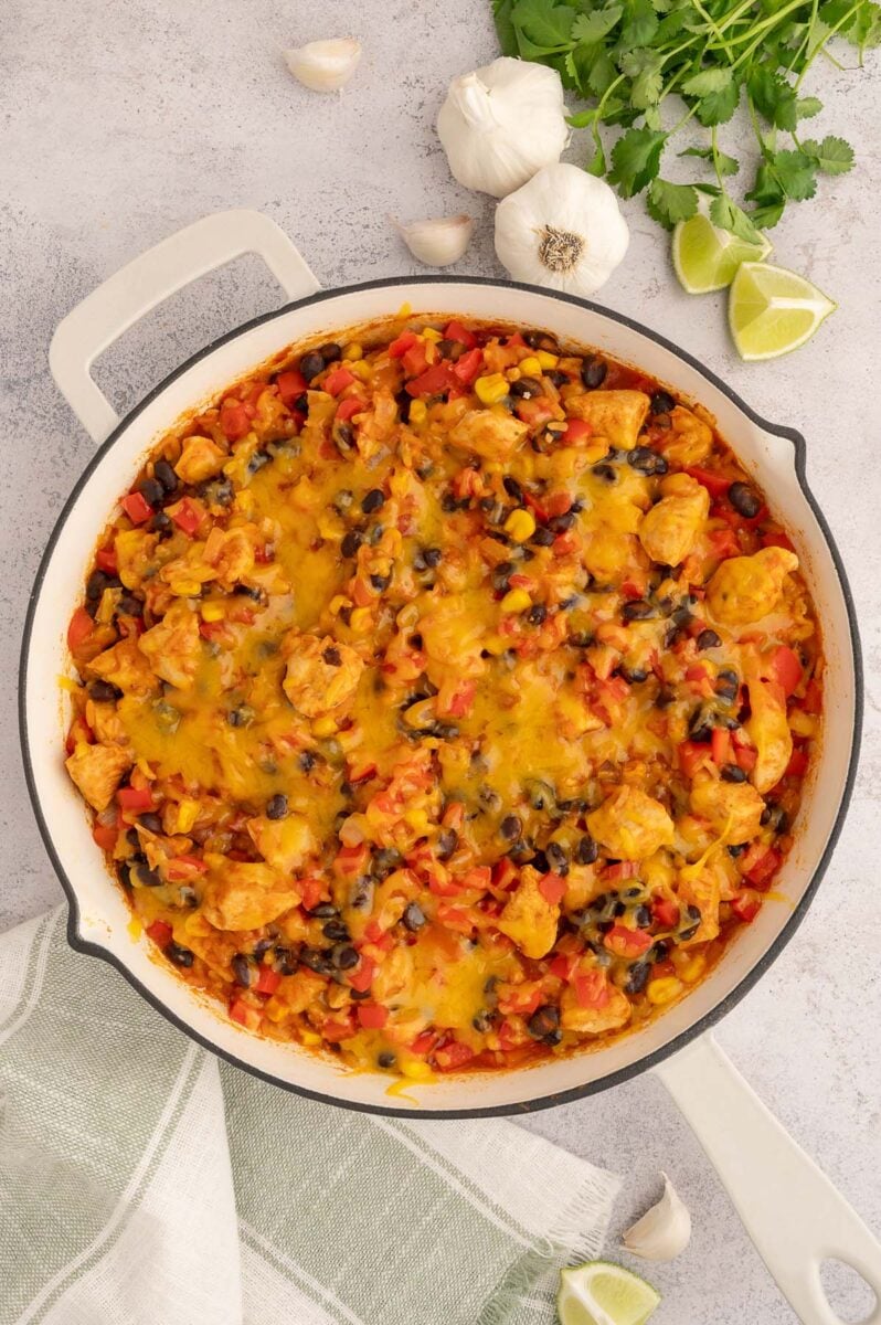 Chicken taco rice skillet with garlic, limes, and cilantro on the side.