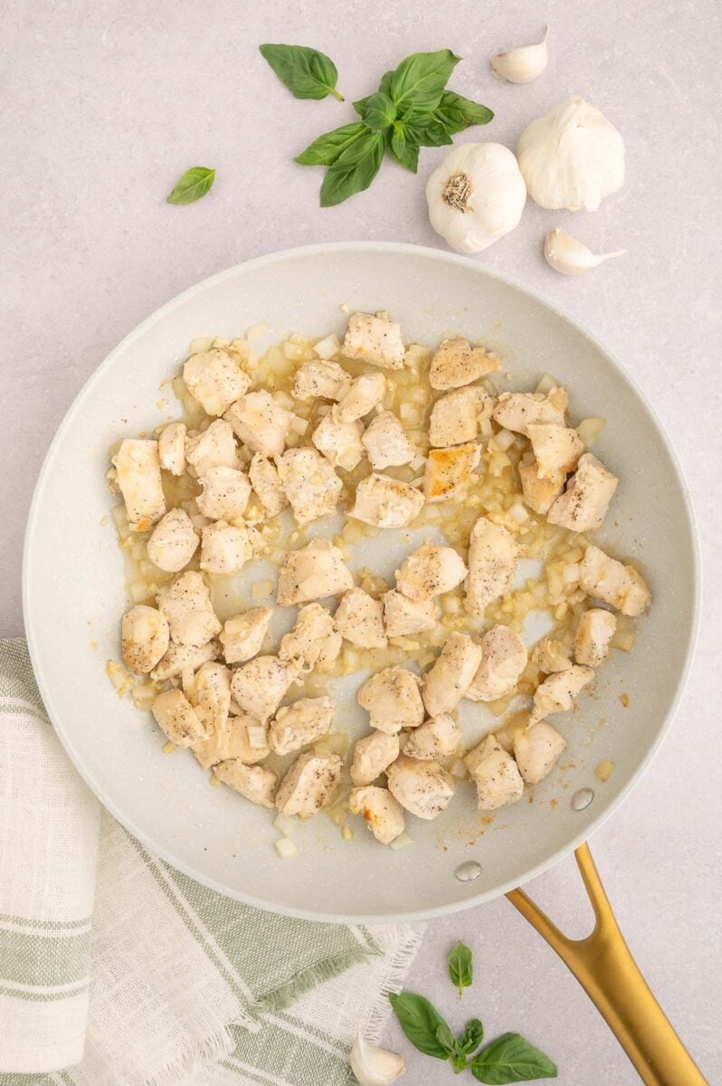 Cubed browned chicken with onions and garlic in a skillet.