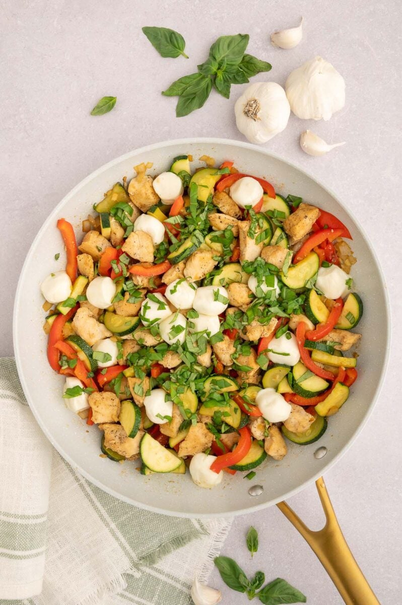 Chicken Vegetable Skillet in a saute pan with basil and garlic on the side.
