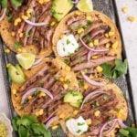 Chili Lime Steak on tacos shells garnished with red onions, cilantro, and corn on a baking sheet.