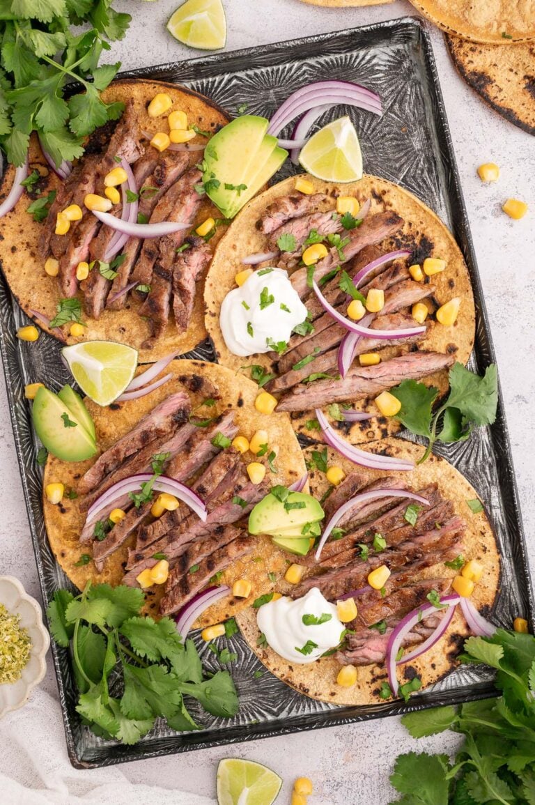 Chili Lime Steak on tacos shells garnished with red onions, cilantro, and corn on a baking sheet.