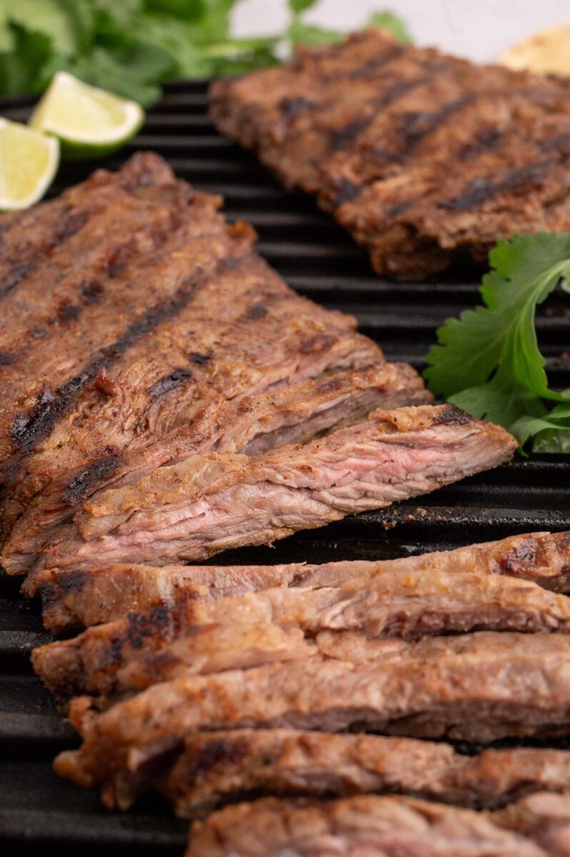 Chili lime steak sliced on a grill pan with another steak in the background.