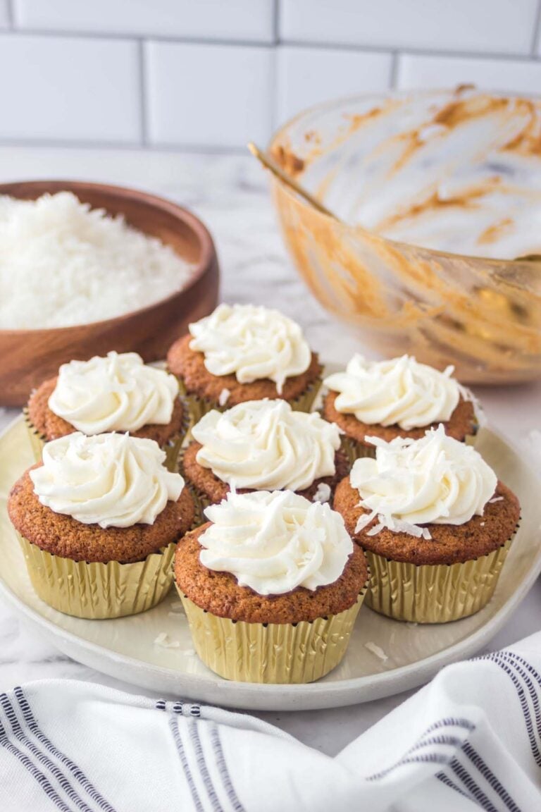 Platter of seven coconut sugar cupcakes topped with swirls of vanilla frosting.