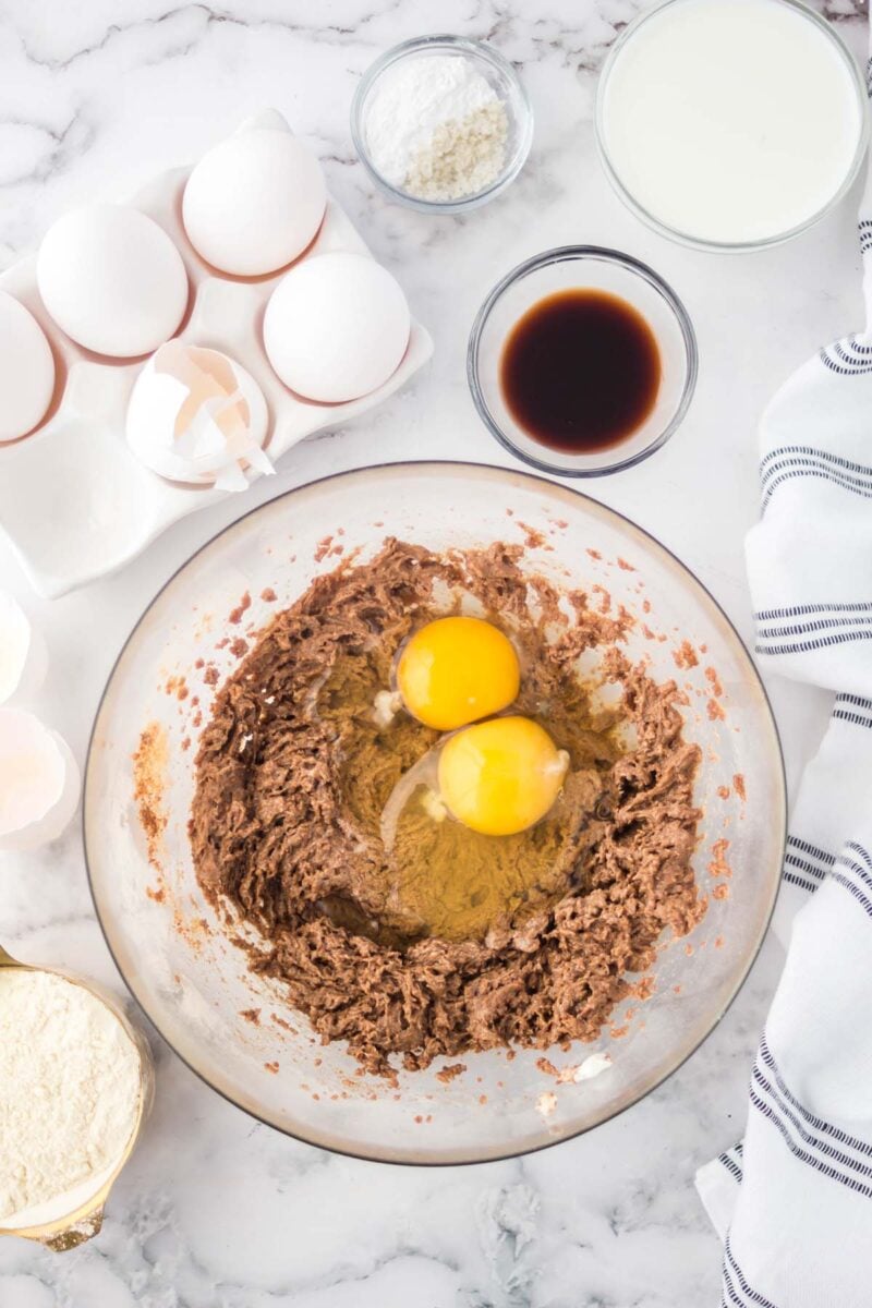 Overhead, looking down into two cracked eggs in a mixing bowl filled with cupcake batter.