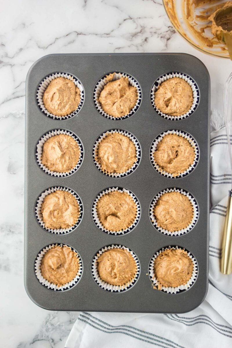 Overhead, looking down on a 12-cup muffin pan holding unbaked batter in paper liners.