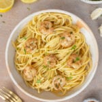 Healthy Shrimp Scampi on a white plate with lemons and herbs on the side.