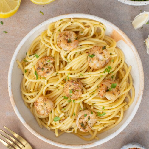 Healthy Shrimp Scampi on a white plate with lemons and herbs on the side.