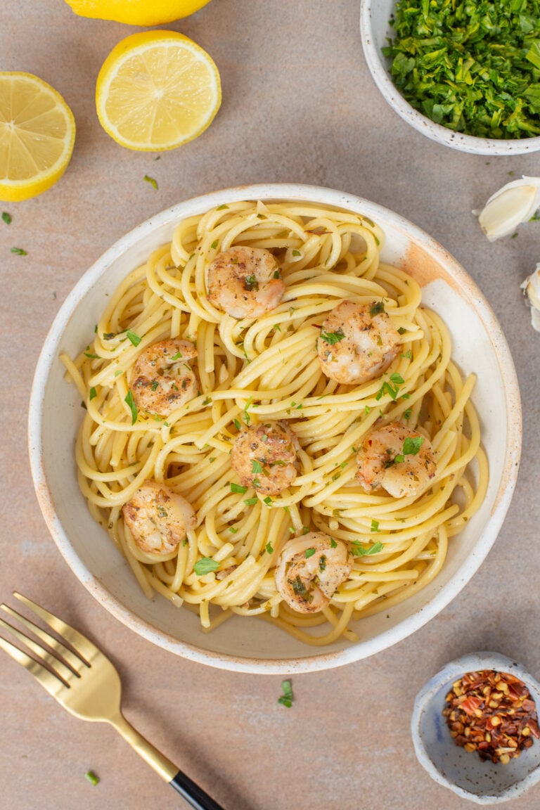 Healthy Shrimp Scampi on a white plate with lemons and herbs on the side.
