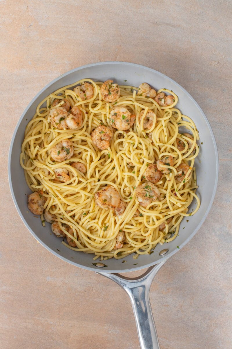 Shrimp scampi tossed with spaghetti in a pan.