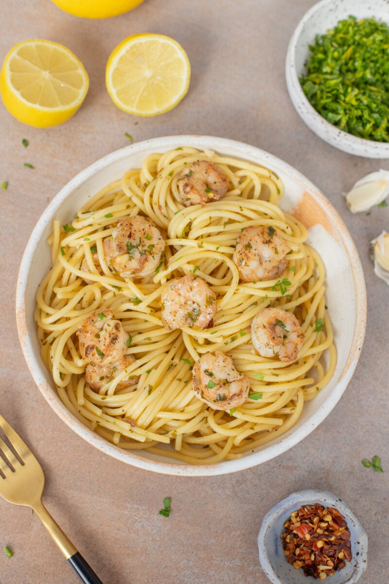 Healthy Shrimp Scampi on a white plate with lemons and herbs on the side.