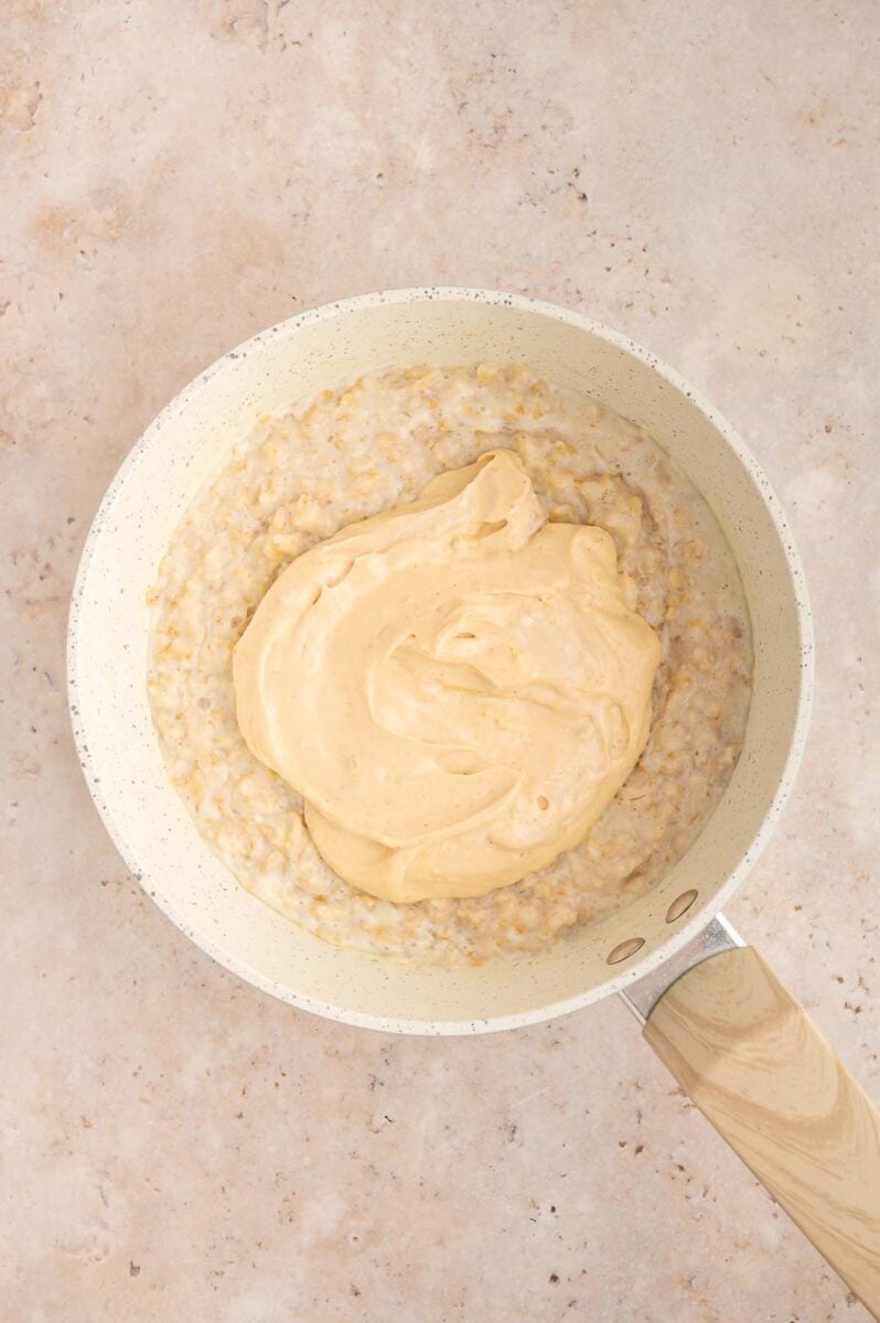 Peanut butter protein yogurt mixture on top of oatmeal in a pot before stirring in.