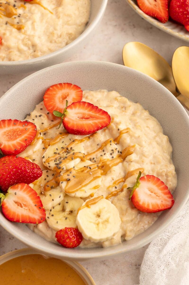 A bowl of protein oatmeal with sliced strawberries and bananas and chia seeds with a drizzle of peanut butter on top.