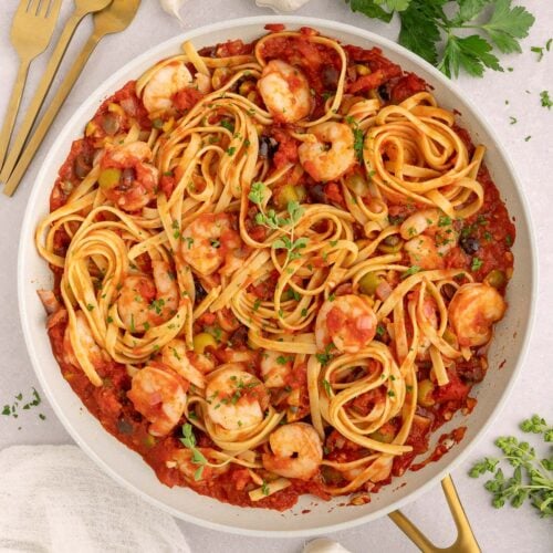 Shrimp Puttanesca in a pan on a countertop with garlic and herbs.