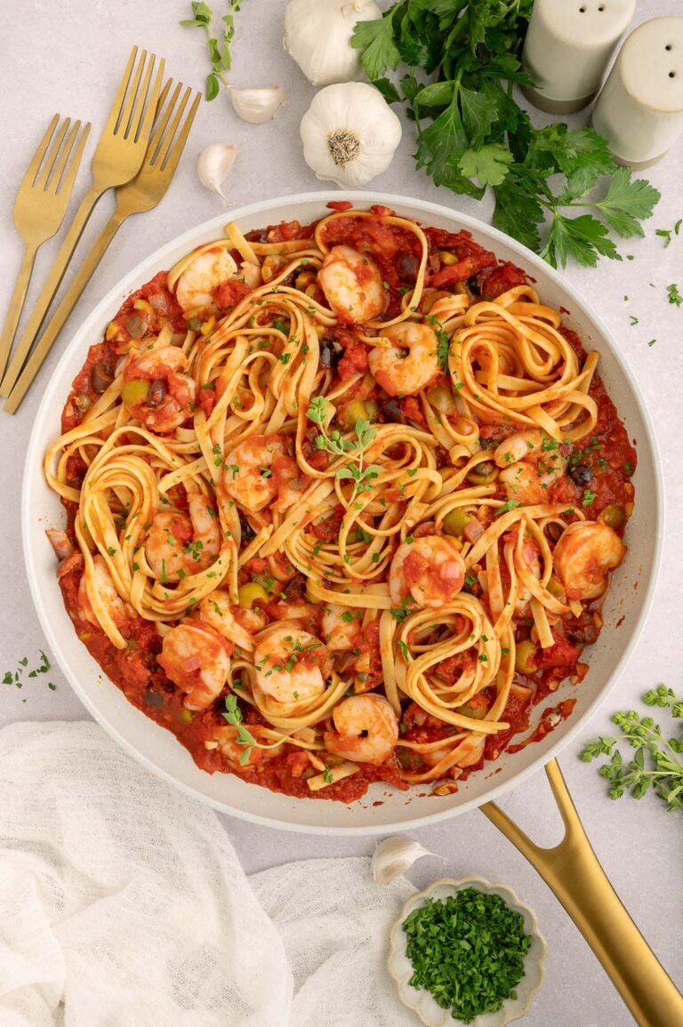 Shrimp Puttanesca in a pan on a countertop with garlic and herbs.