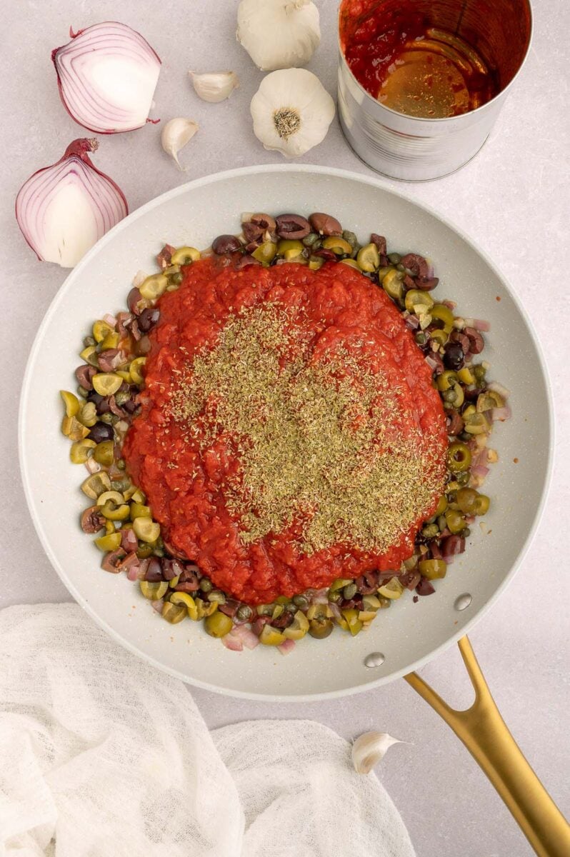 Sauce for shrimp puttanesca in a pan before fully cooking or mixing together with more ingredients on the side. 